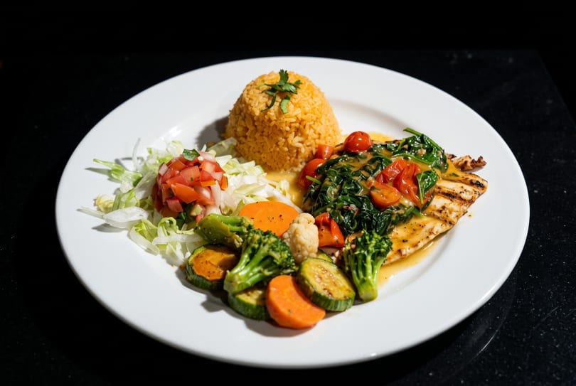 Grilled fish with spinach, cherry tomatoes, rice, mixed vegetables, and a side salad.