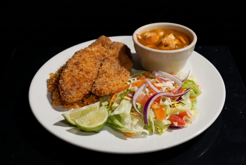 Crispy breaded fish, rice, fresh salad, and shrimp stew served on a white plate.